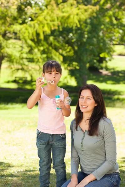 Menina soprando bolhas com sua mãe no parque — Fotografia de Stock