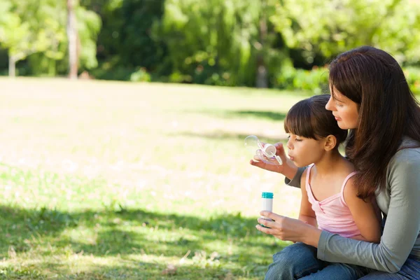 Girl blowing bubbles with her mother in the park — Stock Photo, Image