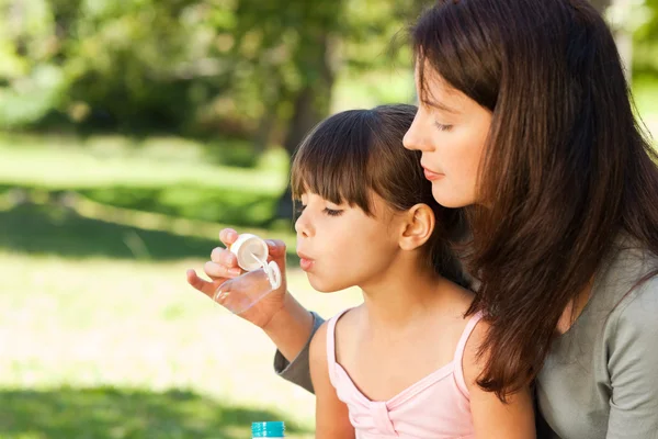 Pige blæser bobler med sin mor i parken - Stock-foto