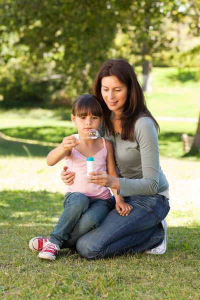 Girl blowing bubbles with her mother in the park — Stock Photo, Image