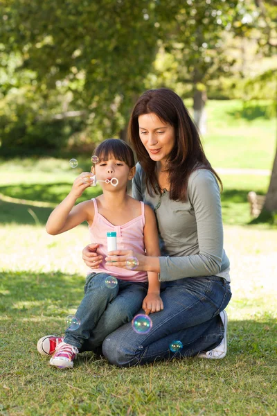Menina soprando bolhas com sua mãe no parque — Fotografia de Stock