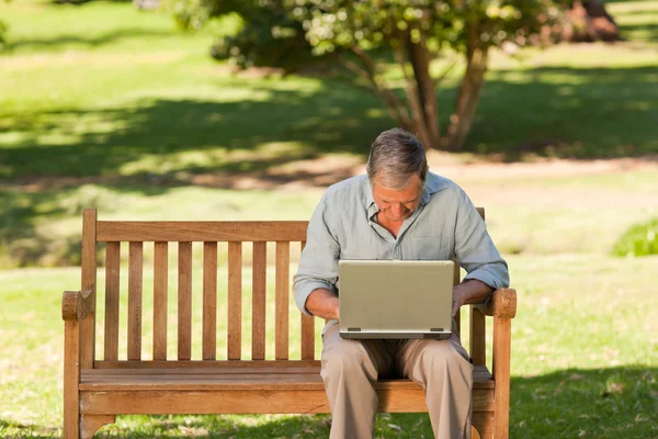 Elderly man working on his laptop in the park — Stock Photo, Image