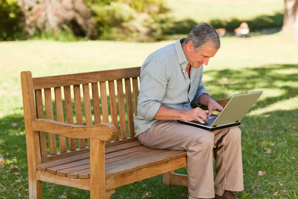 Пожилой человек, работающий над ноутбуком в парке — стоковое фото
