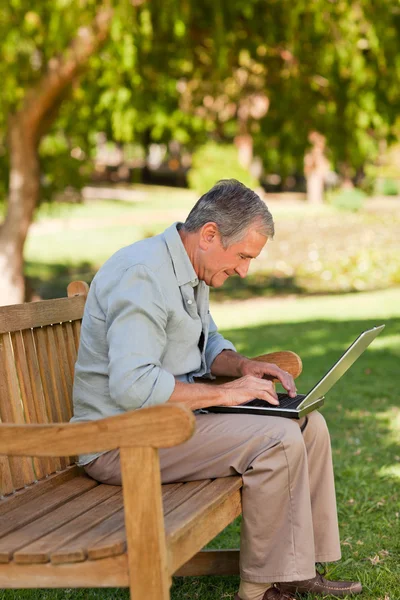 Пожилой человек, работающий над ноутбуком в парке — стоковое фото