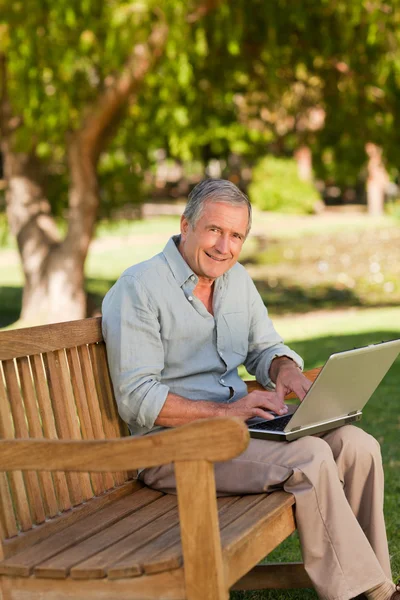 Idoso trabalhando em seu laptop no parque — Fotografia de Stock