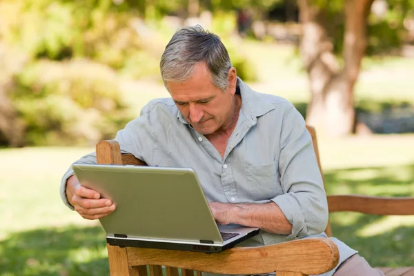 Пенсионер, работающий над ноутбуком в парке — стоковое фото