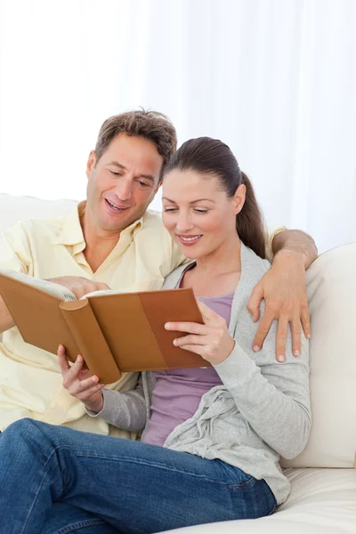 Cute couple looking at a photo album on the sofa — Stock Photo, Image