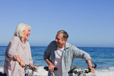 Retired couple with their bikes on the beach clipart