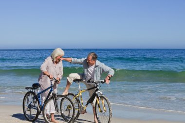 Mature couple with their bikes on the beach clipart