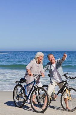 Mature couple with their bikes on the beach clipart