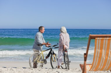 Elderly couple with their bikes on the beach clipart