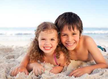 Little boy and his sister lying down on the beach clipart