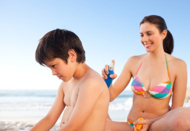 Mother applying sun cream on her son's back clipart