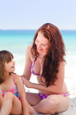 Mother applying sun cream on her daughter's back clipart