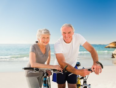 Retired couple with their bikes on the beach clipart