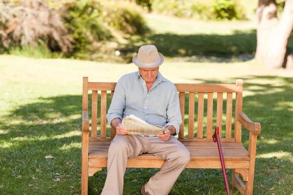 Emeryturze człowiek czytając gazetę na ławce — Zdjęcie stockowe
