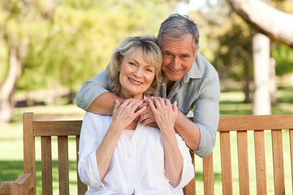 Пожилой мужчина обнимает свою жену, которая сидит на скамейке — стоковое фото