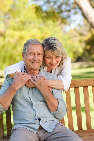 Seniorin umarmt ihren Mann, der auf der Bank sitzt — Stockfoto