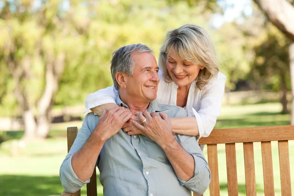 Senior woman hugging her husband who is on the bench — Stock Photo, Image