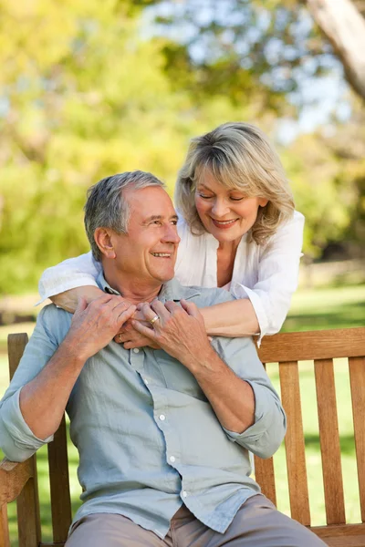 Seniorin umarmt ihren Mann, der auf der Bank sitzt — Stockfoto