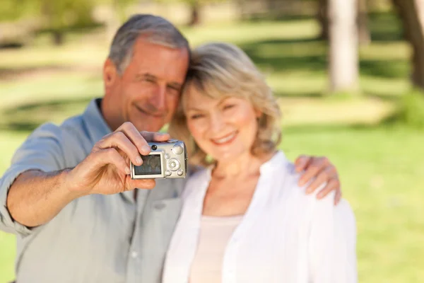 Starší pár, s fotografii sebe v parku — Stock fotografie