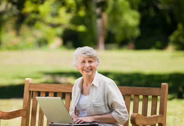 Starsza kobieta pracuje na jej laptopie na ławce — Zdjęcie stockowe