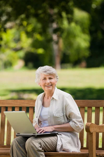 Starsza kobieta pracuje na jej laptopie na ławce — Zdjęcie stockowe