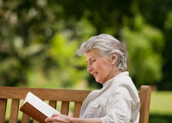Kobieta reired, czytając książkę na ławce — Zdjęcie stockowe