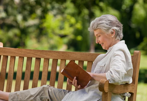 Reired kvinna läser en bok på bänken — Stockfoto