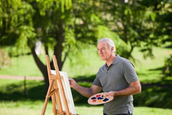 Senior man schilderij in de tuin — Stockfoto