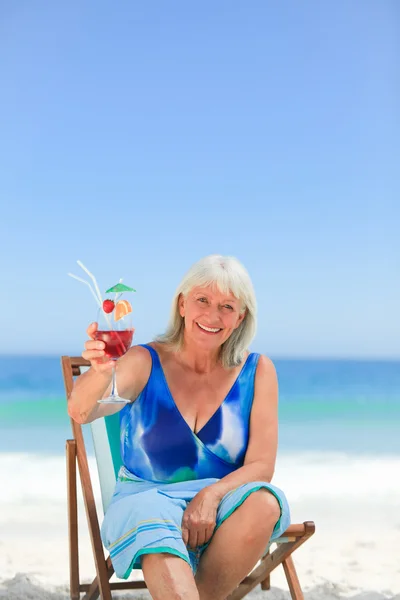 Пожилая женщина пьет коктейль на пляже — стоковое фото
