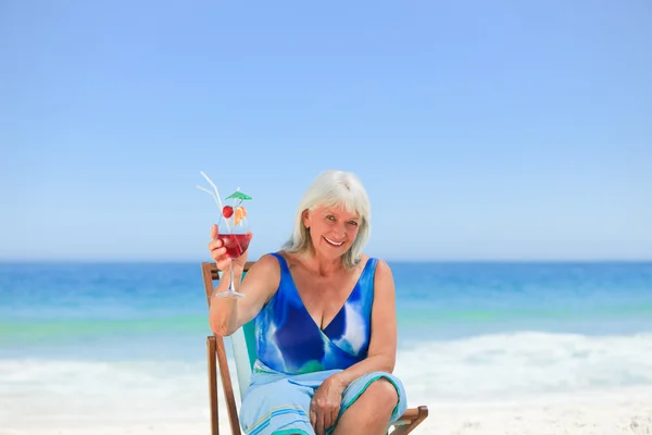 Пожилая женщина пьет коктейль на пляже — стоковое фото