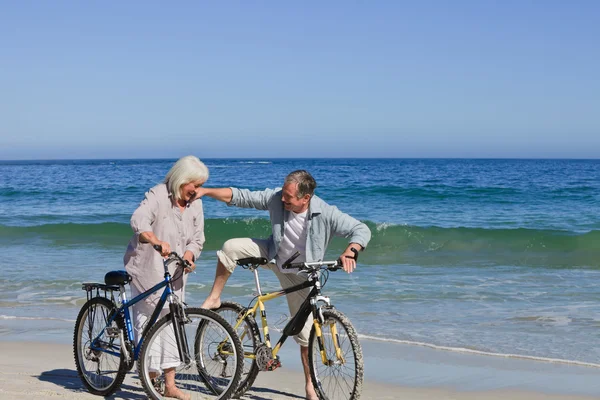 Äldre par med sina cyklar på stranden — Stockfoto