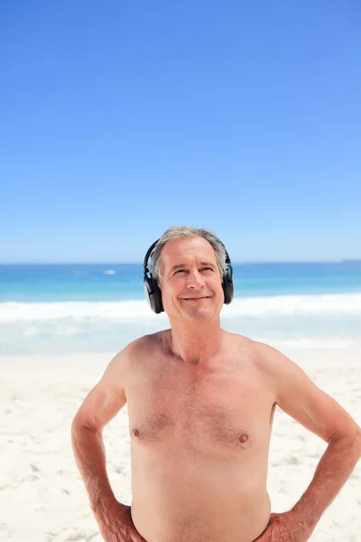 Gepensioneerde man luisteren naar muziek op het strand — Stockfoto