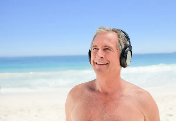 Gepensioneerde man luisteren naar muziek op het strand — Stockfoto