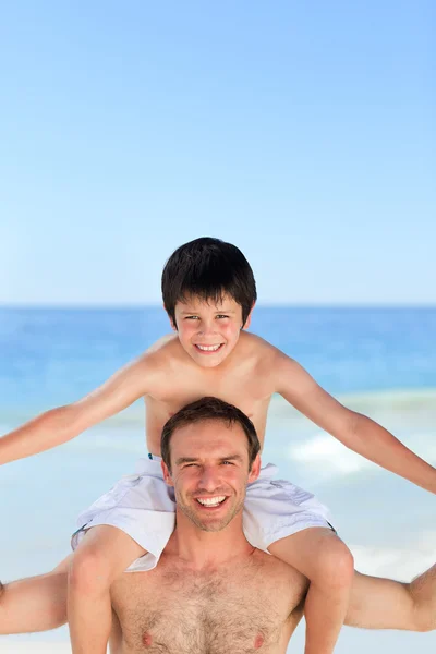 У отца есть сын, который катается на спине по пляжу — стоковое фото