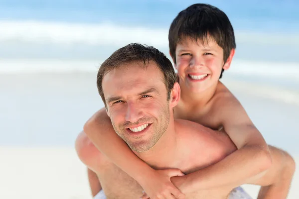 Far med son en piggyback på stranden — Stockfoto