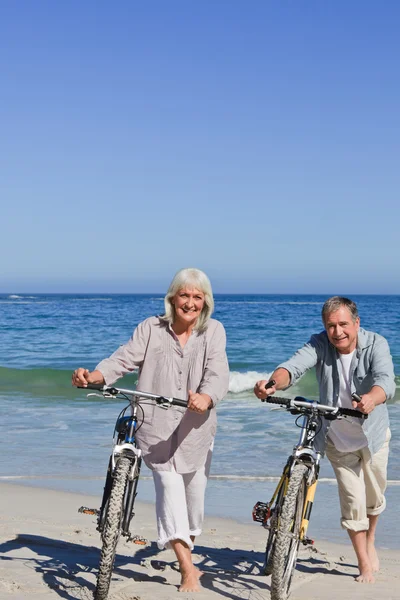 Ältere Paare mit ihren Fahrrädern am Strand — Stockfoto