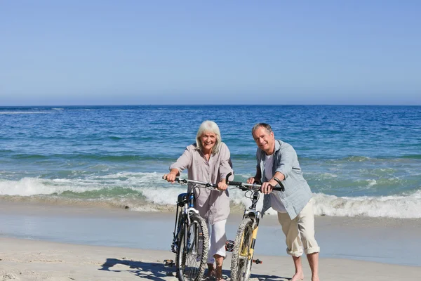 Seniorenpaar mit Fahrrädern am Strand — Stockfoto