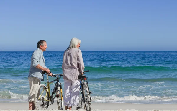 Senior koppel dat met hun fietsen op het strand — Stockfoto