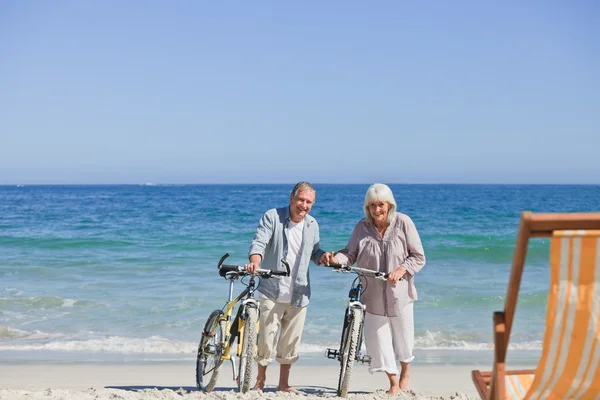 Älteres Ehepaar mit Fahrrädern am Strand — Stockfoto