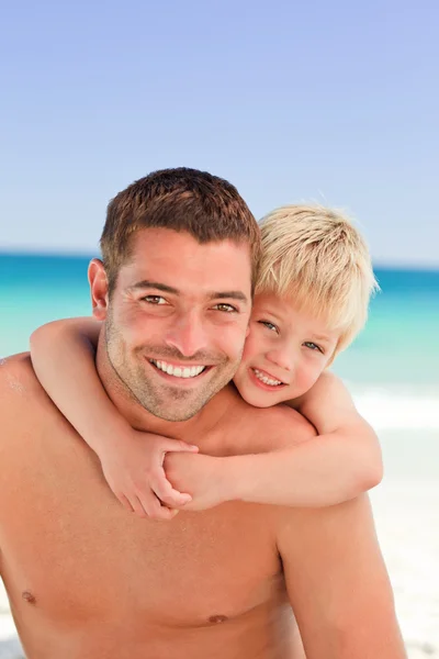 Père souriant ayant un fils un piggyback à la plage — Photo