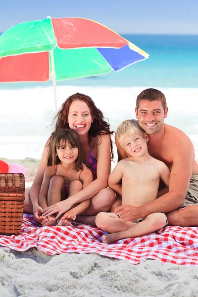 Family picnicking under a sol umbrella on the beach — Stock Photo, Image