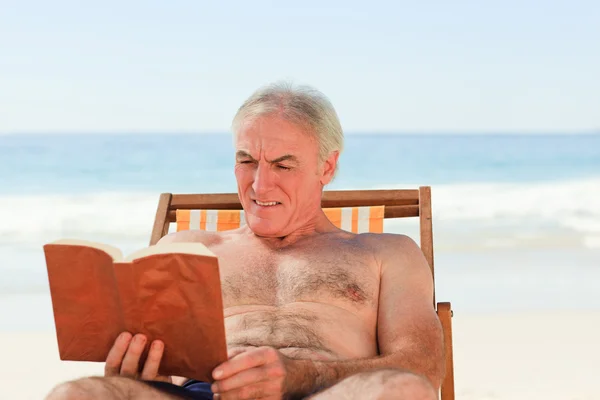 Äldre man läser en bok på stranden — Stockfoto
