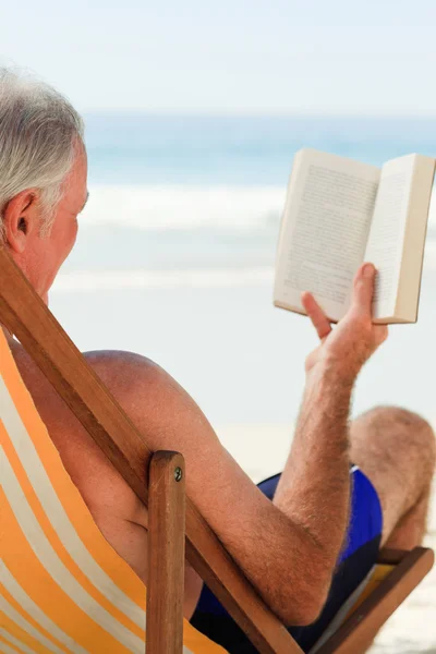 Senior man lezen van een boek op het strand — Stockfoto