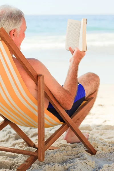 Äldre man läser en bok på stranden — Stockfoto