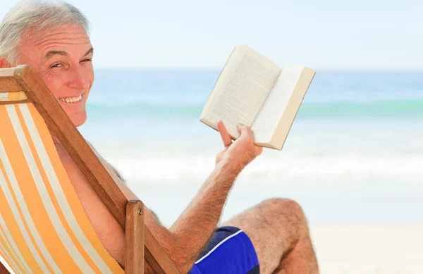 Starší muž s knihou na pláži — Stock fotografie