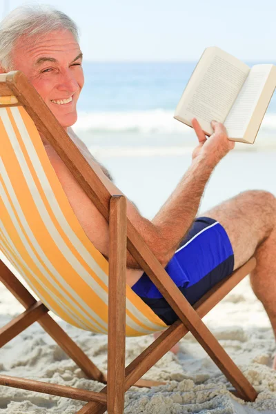 Homem sênior lendo um livro na praia — Fotografia de Stock