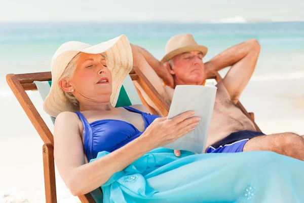Frau liest ein Buch, während ihr Mann am Strand schläft — Stockfoto