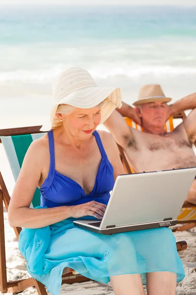Žena pracuje na svém laptopu, zatímco její manžel spí na — Stock fotografie